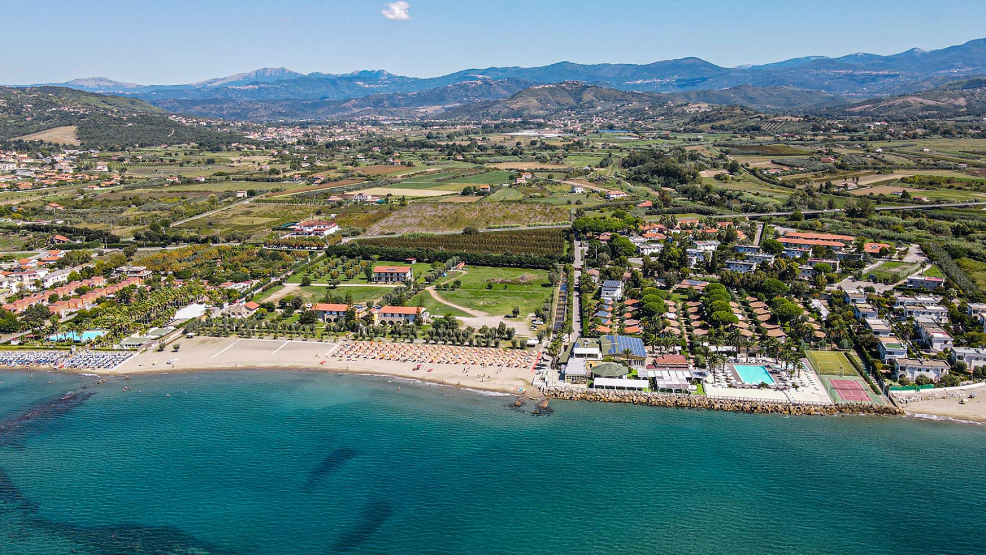 Vista aerea di una spiaggia con ombrelloni e campagna circostante.