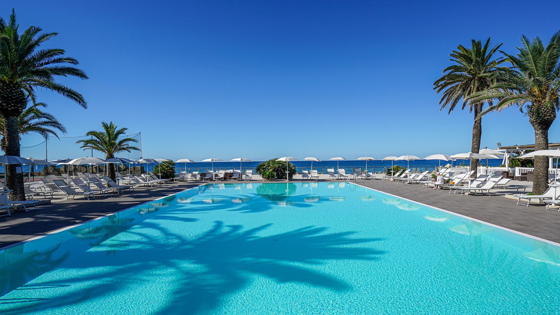 Piscina all'aperto con palme, lettini e vista sul mare.