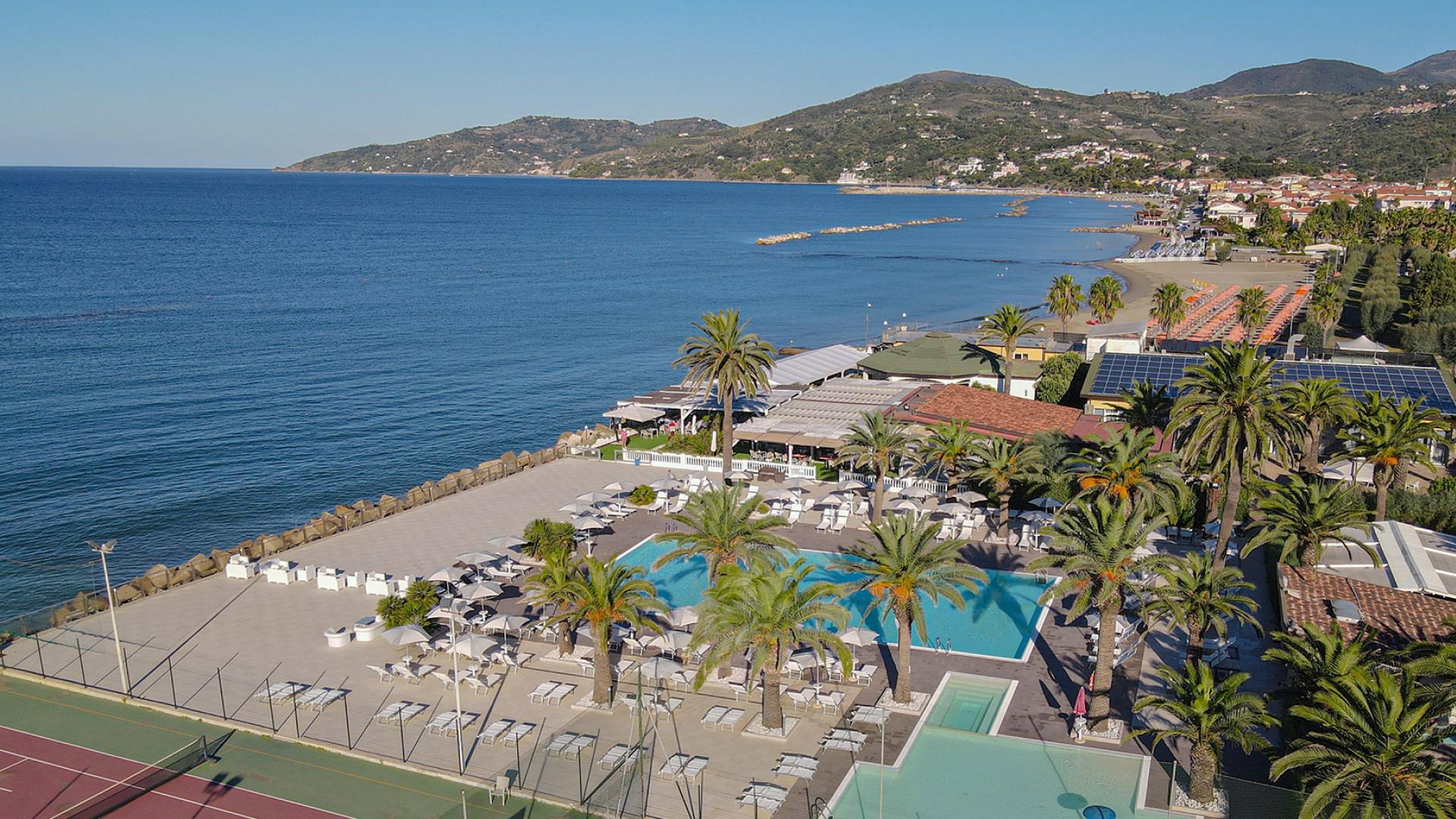 Vista panoramica di una località balneare con piscina, palme e spiaggia.