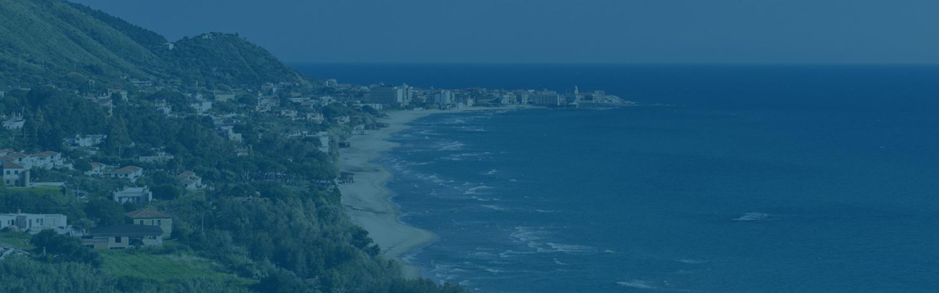 Costa con città e mare, paesaggio verde e colline sullo sfondo.