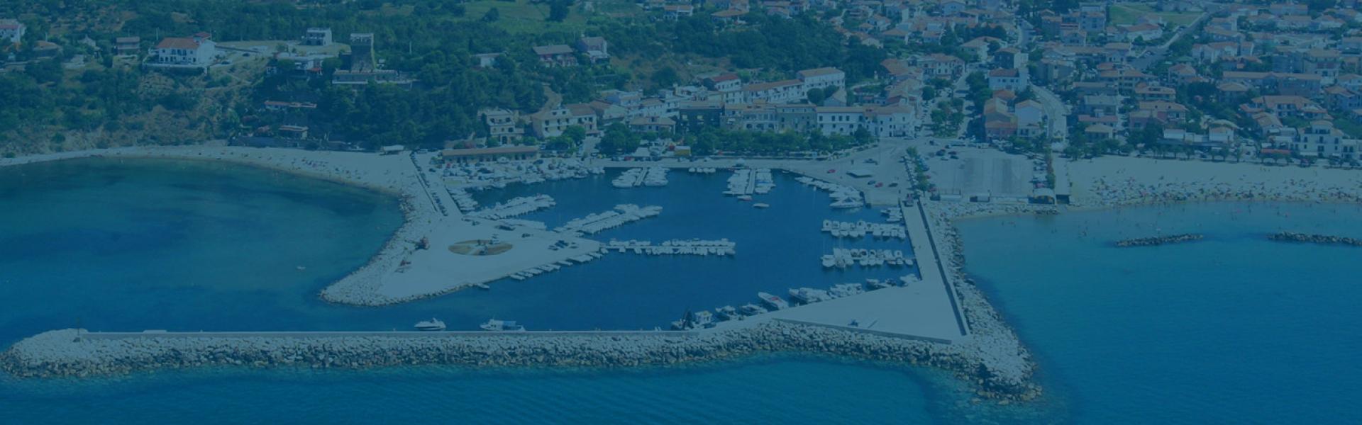 Vista aerea di un porto turistico con spiaggia e città sullo sfondo.