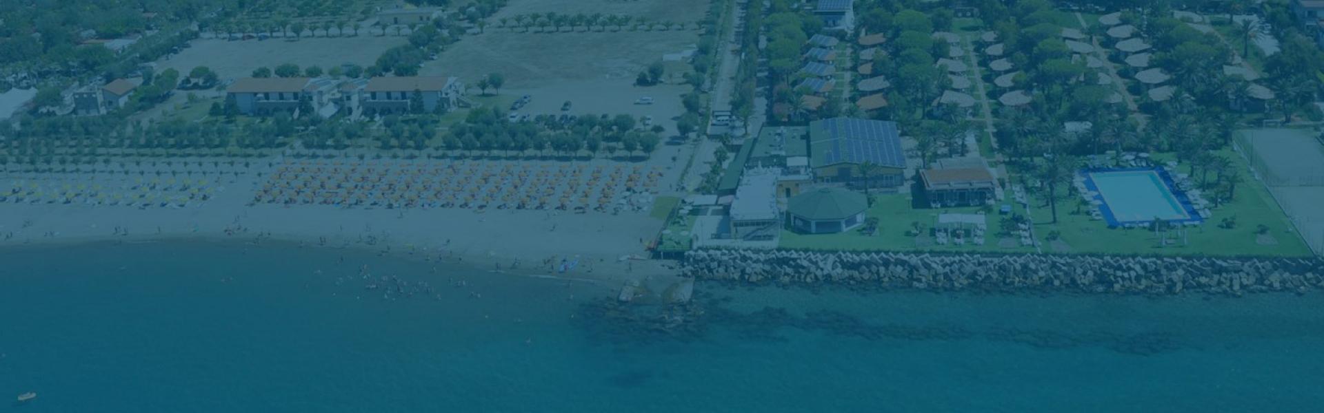 Vista aerea di una spiaggia con ombrelloni, piscina e campi sportivi.