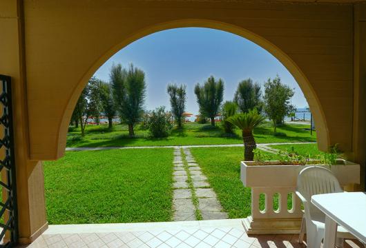 Vista su giardino verde con alberi e sedie sotto un arco.