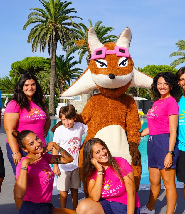 Gruppo di animatori con costume da mascotte, davanti a una piscina con palme.