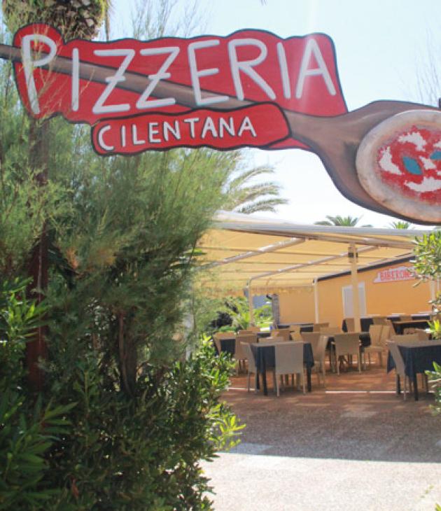 Ingresso di una pizzeria con tavoli all'aperto, insegna 'Pizzeria Cilentana'.