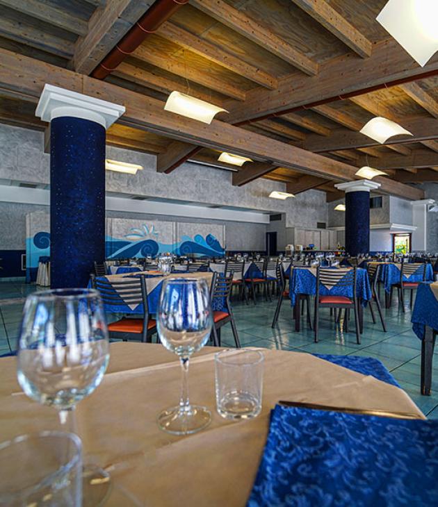 Ristorante elegante con tavoli apparecchiati, soffitto in legno e decorazioni blu.