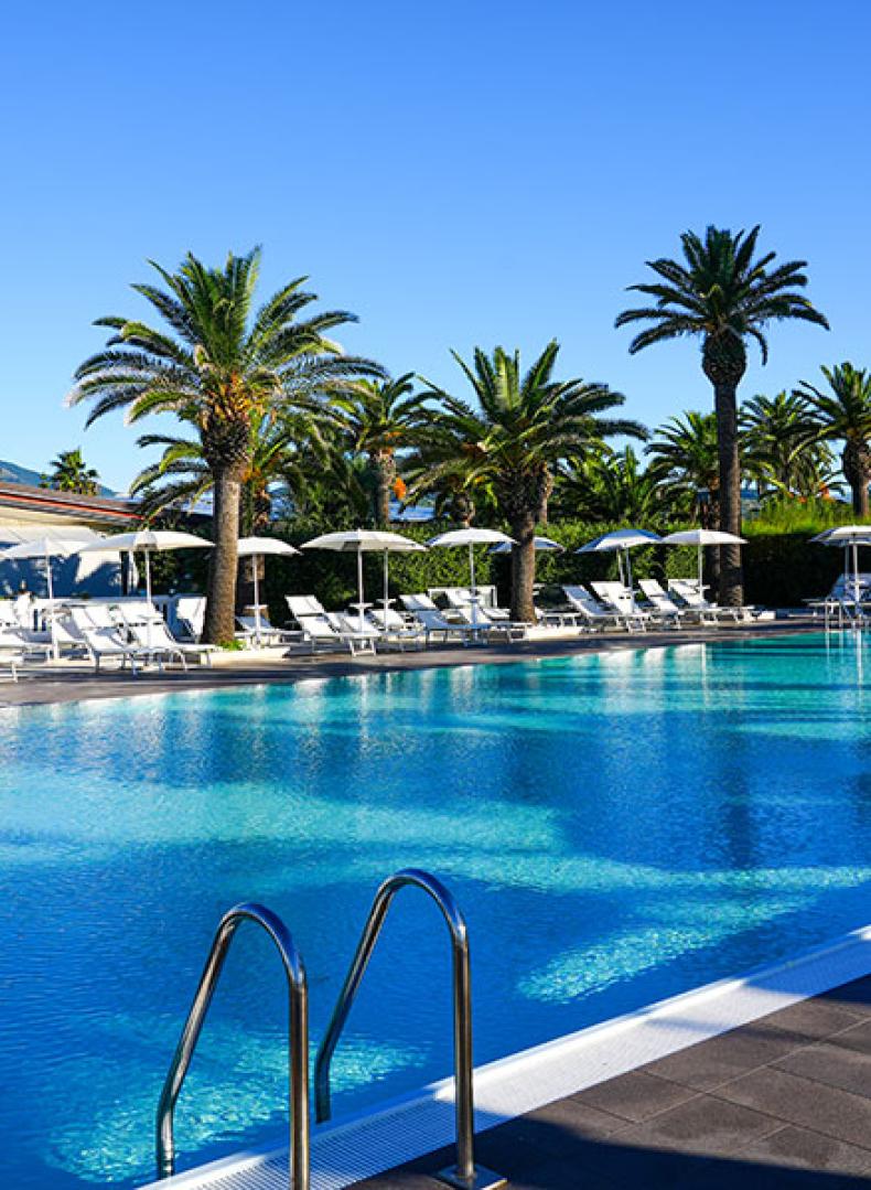 Piscina all'aperto con palme e lettini, cielo sereno e ambiente rilassante.