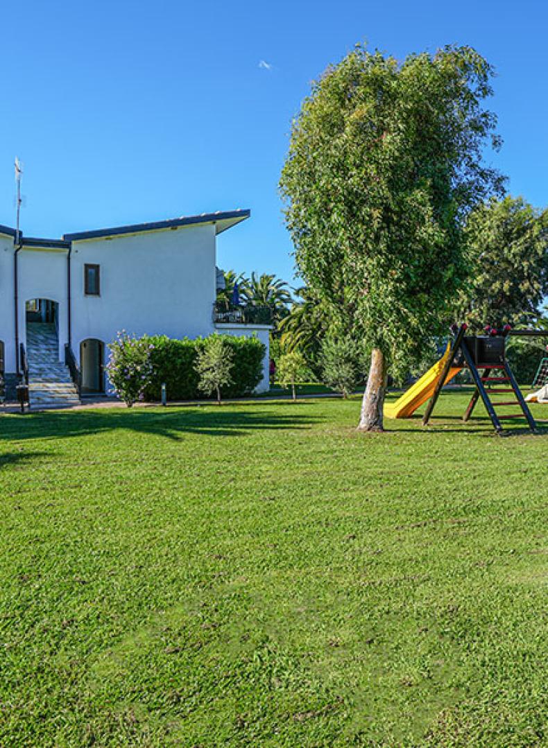 Giardino con prato, altalena e scivolo, davanti a una casa moderna.