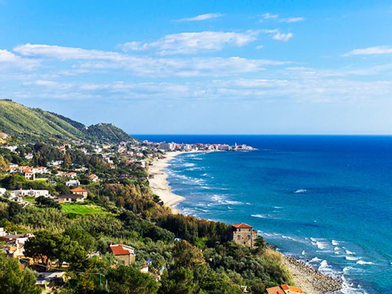 Vista panoramica di una costa con mare azzurro e colline verdi.