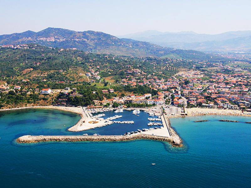 Vista aerea di un porto turistico con montagne e città sullo sfondo.