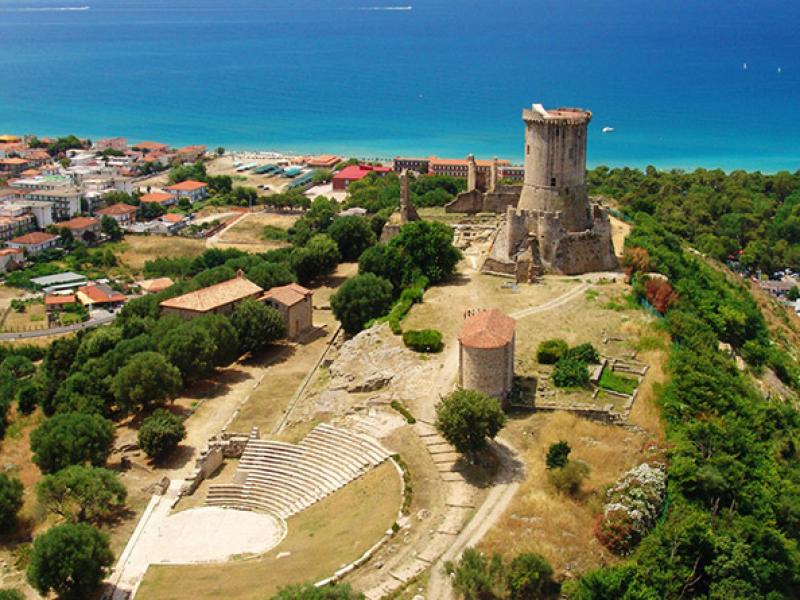 Vista aerea di una torre e anfiteatro antico vicino al mare.