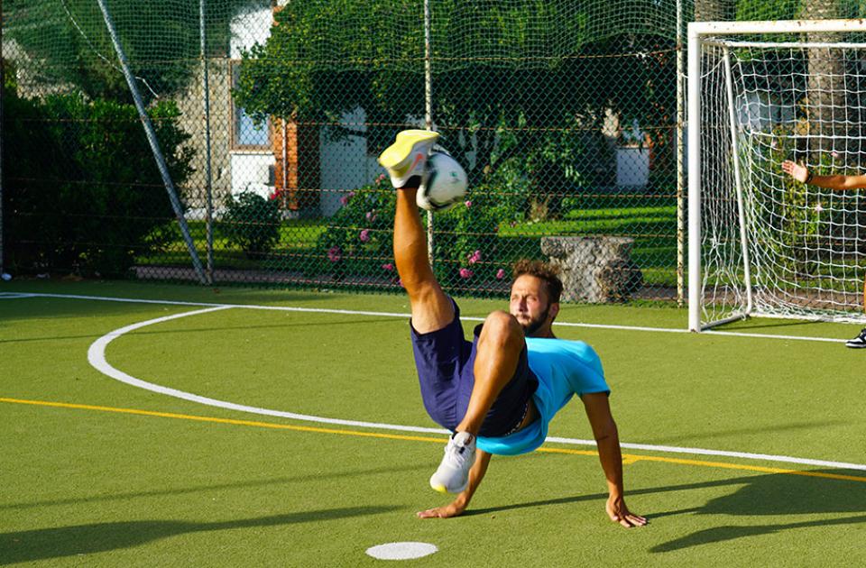 Calciatore esegue acrobazia, portiere pronto a parare sul campo da calcio.