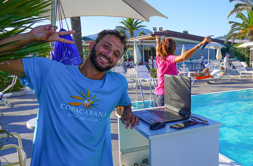 Uomo sorridente vicino alla piscina di un hotel, con palme e lettini.