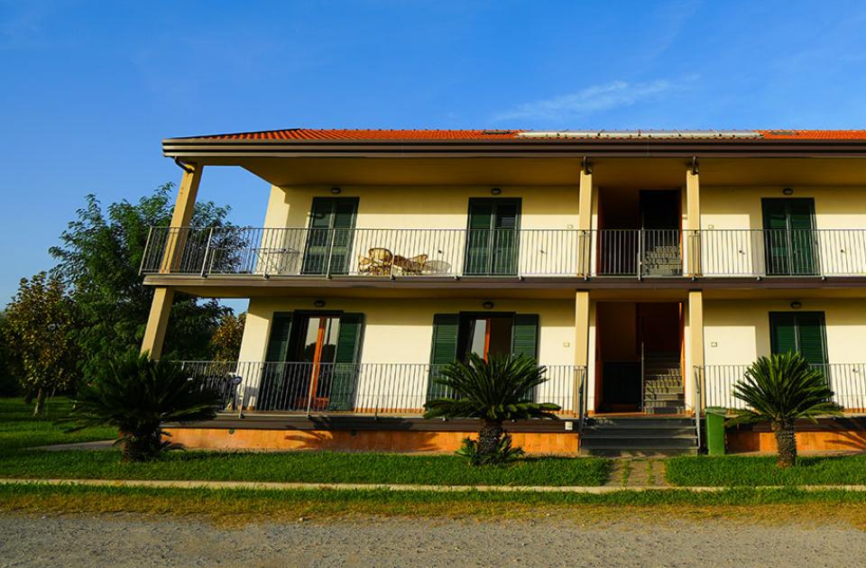 Edificio a due piani con balconi e giardino, cielo sereno sopra.