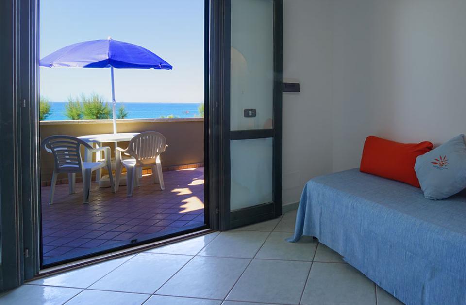 Appartamento con terrazza vista mare, divano letto e ombrellone blu.