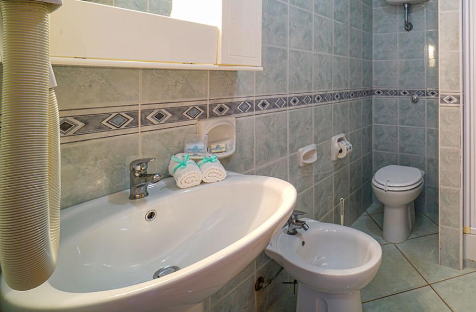 Bagno con lavabo, bidet, WC, doccia e asciugamani su piastrelle blu e bianche.