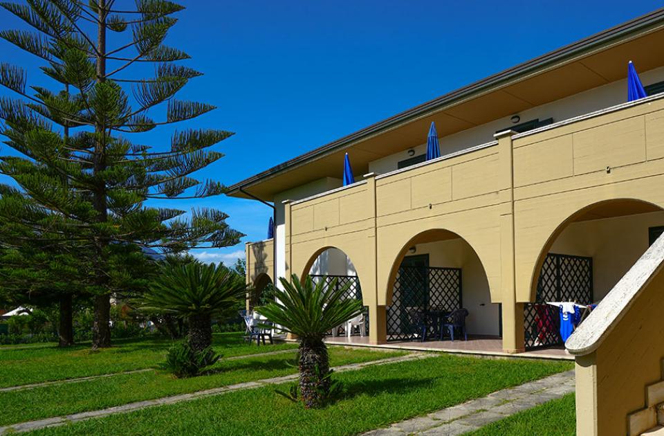 Edificio a due piani con archi, scale esterne e giardino verde.