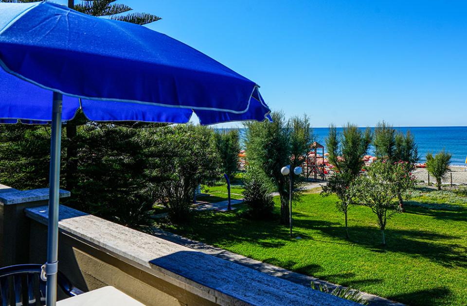 Vista mare con ombrellone blu e giardino verde.