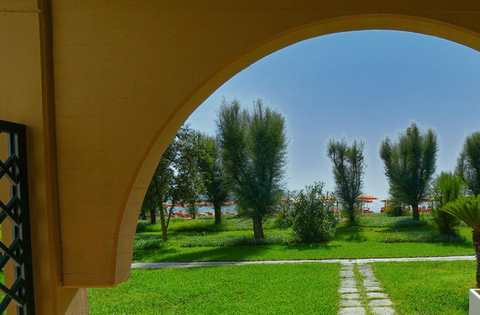 Vista di un giardino con alberi e ombrelloni attraverso un arco.