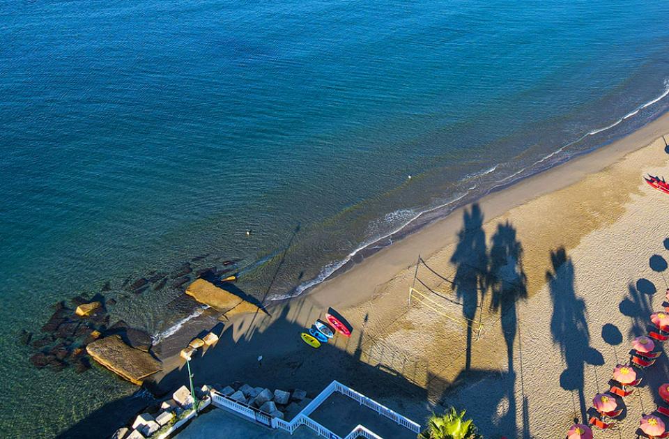 Spiaggia con ombrelloni arancioni, mare calmo e ombre di palme al tramonto.