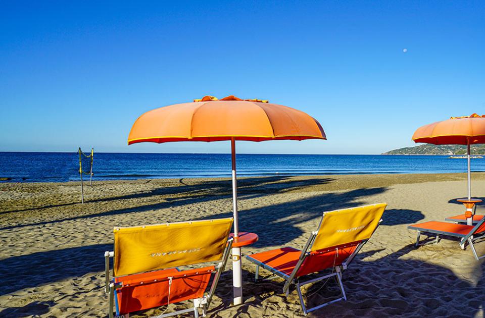 Spiaggia con ombrelloni arancioni e lettini, mare calmo e cielo limpido.