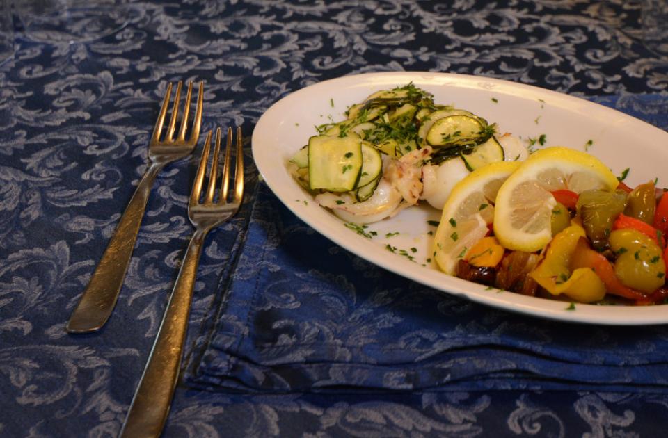 Piatto di verdure grigliate con fette di limone e zucchine, apparecchiato elegantemente.