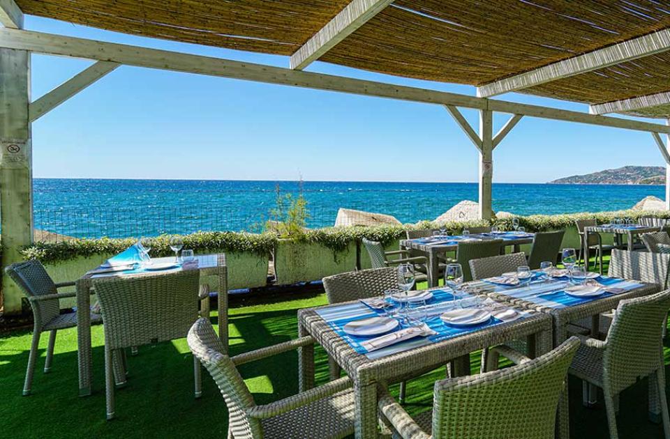 Ristorante all'aperto con vista mare, tavoli apparecchiati sotto una pergola.