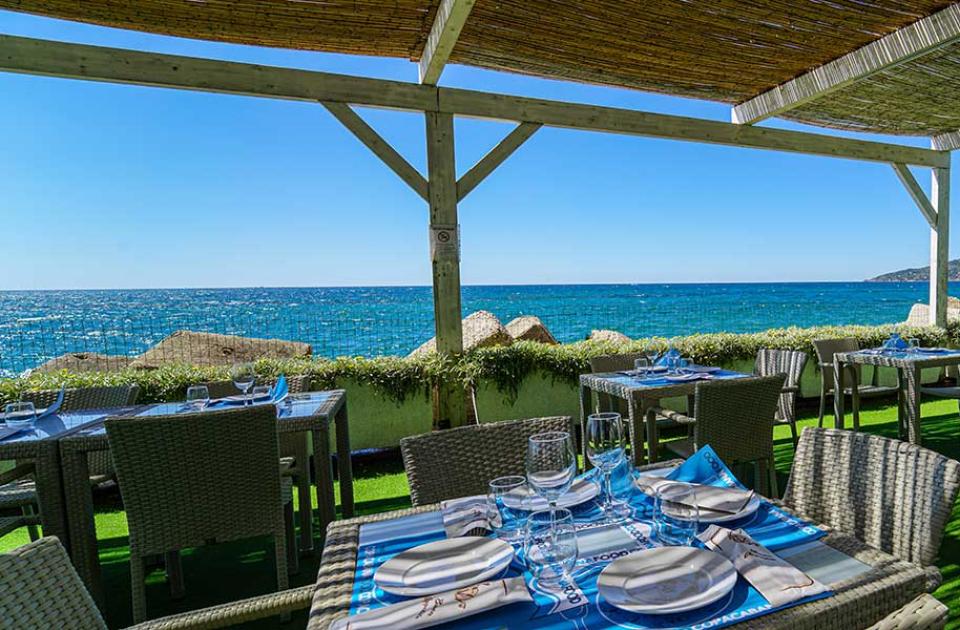 Ristorante all'aperto con vista mare, arredamento elegante e atmosfera rilassante.