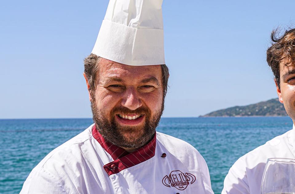 Due uomini sorridenti, uno chef e un cameriere, davanti al mare.