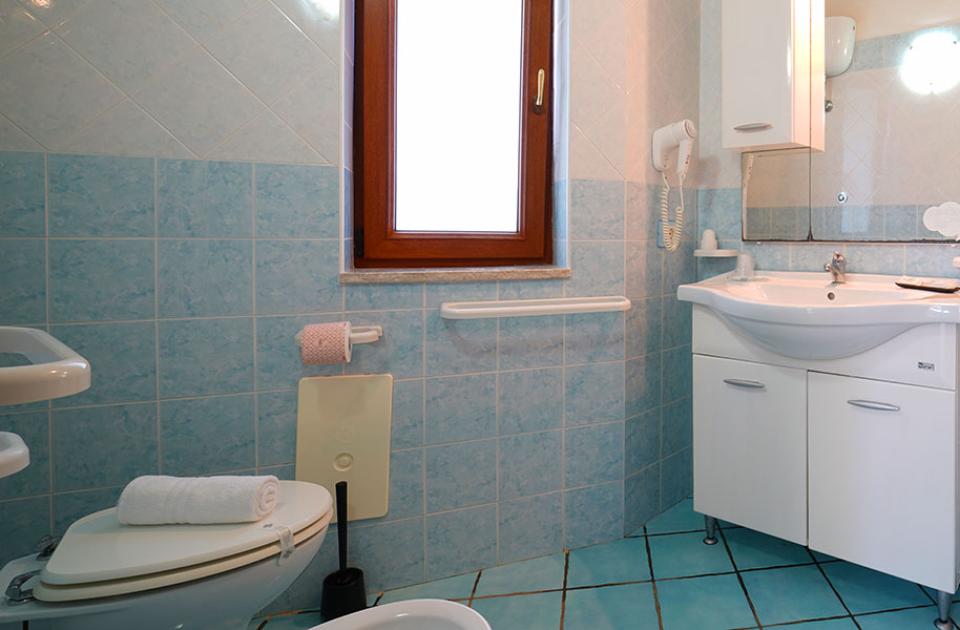 Bagno con piastrelle azzurre, lavabo bianco e doccia con porta scorrevole.