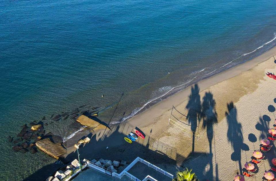 Spiaggia con ombrelloni arancioni allineati e mare calmo, vista dall'alto.