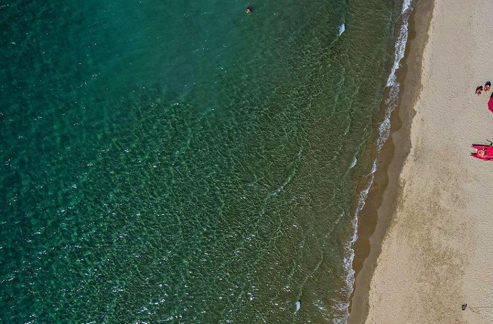 Spiaggia con ombrelloni colorati e mare cristallino, vista dall'alto.