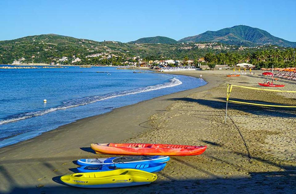 Spiaggia con ombrelloni arancioni, kayak colorati e vista su montagne verdi.