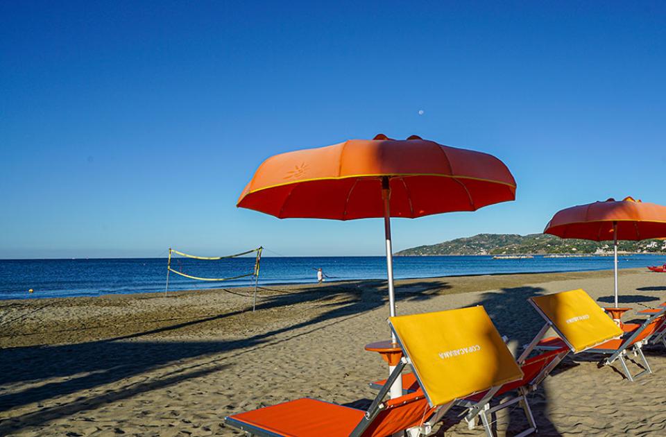 Spiaggia con ombrelloni arancioni, lettini e mare calmo sotto un cielo limpido.