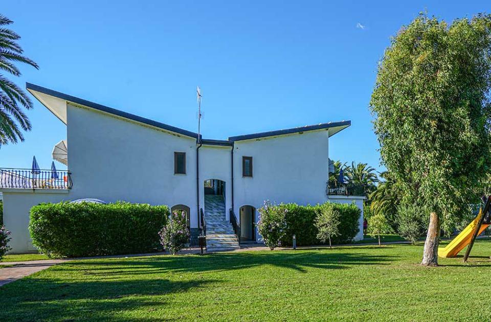 Casa moderna con giardino ampio, altalena e palme.